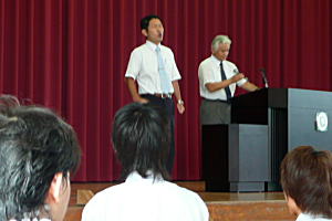 ステージで校歌を独唱される先生、後ろは音楽の先生